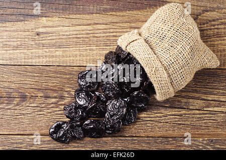 Getrocknete Pflaumen in kleine Sack auf alten Holztisch. Ansicht von oben Stockfoto