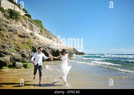 glückliches Paar Hand in Hand laufen am Strand in der Nähe von Meer in Hochzeitstag Stockfoto