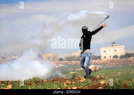 Nabi Saleh, West Bank. 6. Februar 2015. Eine maskierte palästinensische Demonstranten verwendet eine Schleuder, um wieder einen Kanister Tränengas auf israelische Truppen während der Zusammenstöße bei einer wöchentlichen Protest gegen jüdische Siedlungen im Westjordanland-Dorf von Nabi Saleh, in der Nähe von Ramallah schleudern. © Shadi Hatem/APA-Images/ZUMA Draht/Alamy Live News Stockfoto