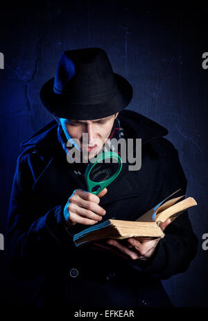Mann mit schwarzem Hut mit Lupe, die das alte Buch bei dunklem Hintergrund Stockfoto