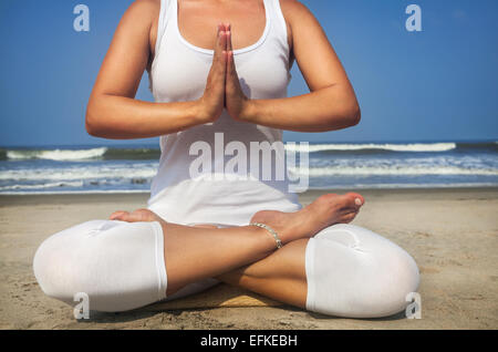 Frau tut Yoga Meditation im weißen Kostüm am Strand von Goa, Indien Stockfoto