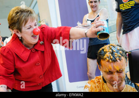 Lokalen Komödiantin und Schauspieler/Schauspielerin Olivia Nash hilft bei Comic Relief Red Nose Day durch strömenden Bohnen über einen Mann, eine Bohne Bad zu nehmen. Stockfoto