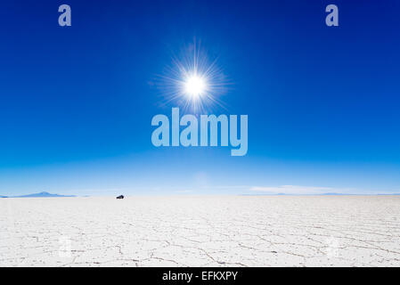 Blick auf die Sonne über den Salt Flats Uyuni in Bolivien mit einem SUV in den Hintergrund. Stockfoto