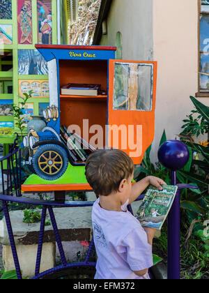 Ein kleiner Junge hält ein Buch, das er nur aus einer kleinen freien Bibliothek gebaut in der Form eines altmodischen Autos ausgewählt. Stockfoto