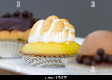 Ausschank von drei kleinen Desserts auf einem weißen Teller mit einer Zitronen-Baiser im Fokus Stockfoto