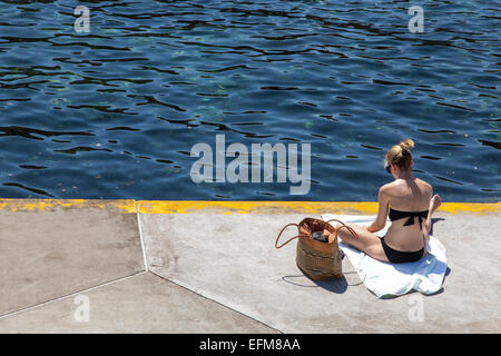 Frau sitzt auf einer Betonplattform auf Clovelly Beach, Sydney, New South Wales, Australien Stockfoto