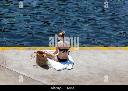 Frau sitzt auf einer Betonplattform auf Clovelly Beach, Sydney, New South Wales, Australien Stockfoto