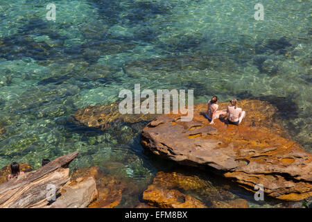 Frauen sitzen auf einem Felsen in Gordons Bay, Sydney, Australien Stockfoto