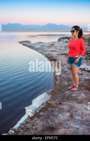 Frau steht am Rand der Lagune Salz-verkrusteten Ufer des Tebenquiche bei Sonnenuntergang, San Pedro de Atacama Wüste, Chile, Südamerika Stockfoto