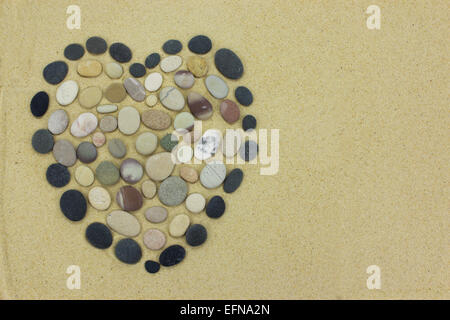 Herzform aus Strand Steinen oder Kiesel auf goldenem Sand hergestellt. Stockfoto