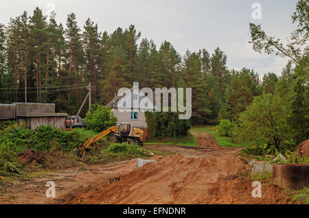 Straßenbau. Der Baumeister am Bagger gräbt Sand für die Brücke - ein Rohr über einen Stream. Stockfoto