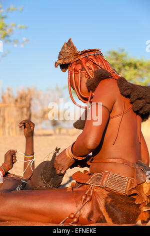 Eine Himba-Frau macht traditionelle Zöpfe auf ein junges Mädchen, Namibia. Stockfoto