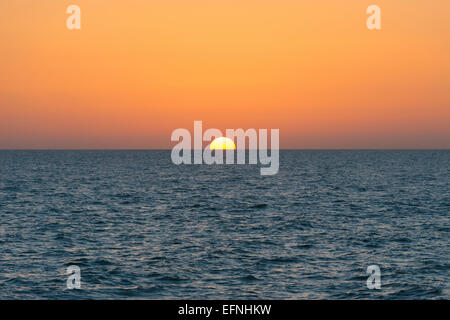 Die Sonne am Horizont mit dem Meer im Vordergrund Stockfoto