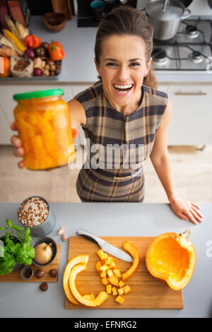 Porträt der glückliche junge Hausfrau zeigt Glas mit eingelegter Kürbis Stockfoto