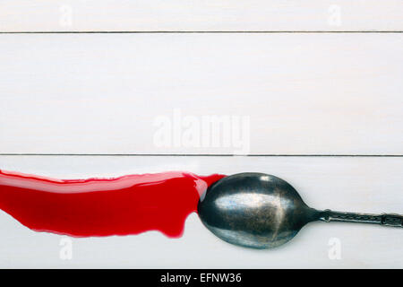 Flecken von roter Saft fließt nach unten vom Löffel auf weißem Holz Hintergrund mit Platz für text Stockfoto