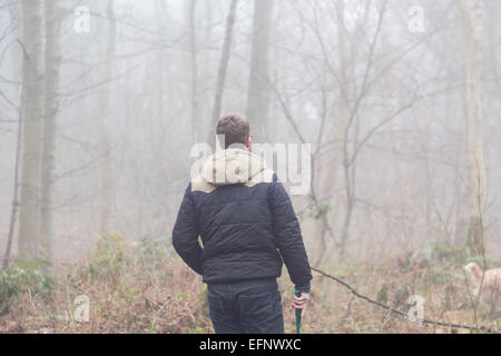 Ein Mann geht mit seinem Hund in nebligen Wäldern Stockfoto