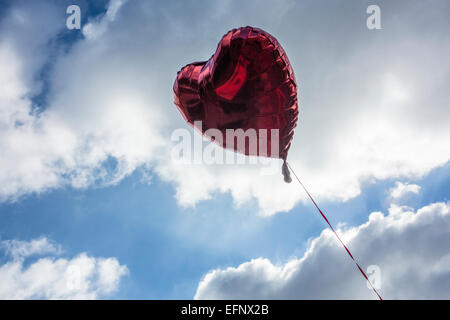 Ein rotes Herz geformt Helium-Ballon in einem blauen Wolkenhimmel Stockfoto
