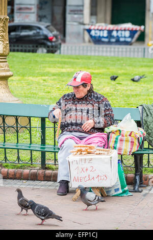 Lokale Lebensstil: armen alten Frau bag Lady auf einer Parkbank verkaufen Erdnüsse Tauben auf der Plaza de Mayo, in der Innenstadt von Buenos Aires, Argentinien zu füttern Stockfoto