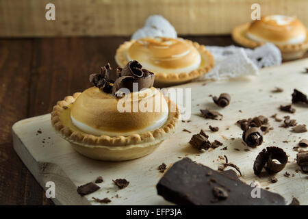 Zitronenkuchen und italienische Meringue, dekoriert mit Schokolade locken auf orangem Hintergrund Holz Stockfoto