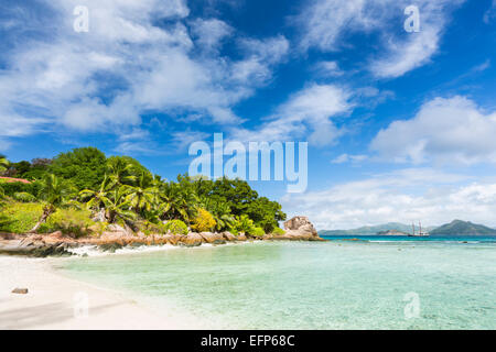 Ruhiges Wasser am Anse Severe in La Digue, Seychellen mit Palmen und Granit Felsen im Hintergrund Stockfoto