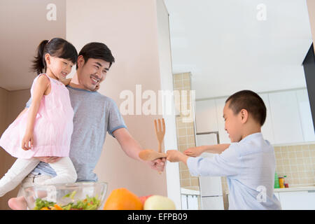 Vater und Kinder fechten in Küche Stockfoto