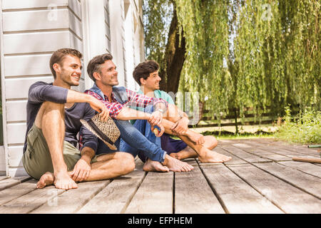 Drei Männer sitzen auf hölzernen Terrassendielen, wegschauen Stockfoto