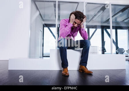 Reifer Mann sitzt auf Podest mit Kopf in Händen Stockfoto