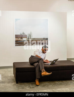 Junger Mann sitzt mit einem Laptop-Computer in einer Kunstgalerie, Phnom Penh, Kambodscha. Stockfoto