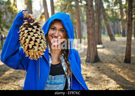 Porträt der jungen Frau im Wald hält große Tannenzapfen, Los Angeles, Kalifornien, USA Stockfoto