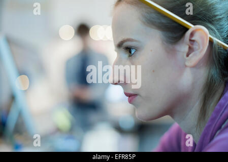 Eine junge Frau mit einem Bleistift hinter ihr Ohr an eine Computer-Werkstatt. Stockfoto