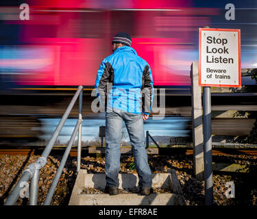 Mann steht auf ländlichen Bahnübergang als Zug vorbei an Geschwindigkeiten Stockfoto