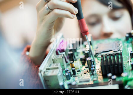 Eine Frau mit einer elektronischen Schraubendreher auf einem Computer-Leiterplatte. Stockfoto