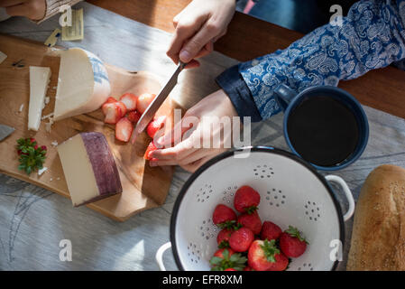 Eine Frau, die Erdbeeren auf einem Tisch mit einem Schneidbrett aus Holz mit einer Auswahl an Käse und Brot schneiden. Stockfoto
