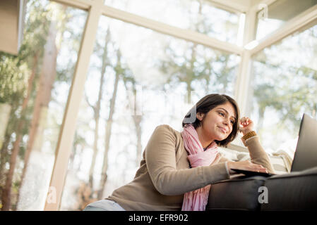 Frau sitzt auf dem Boden vor einem Sofa Blick auf ihrem Laptop. Stockfoto