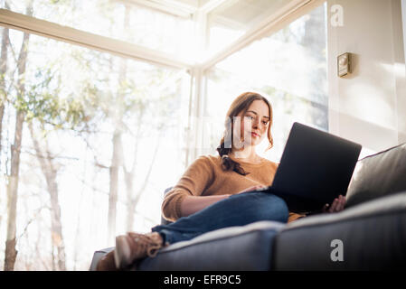 Niedrigen Winkel Blick auf eine Frau sitzt auf einem Sofa, Blick auf ihrem Laptop. Stockfoto