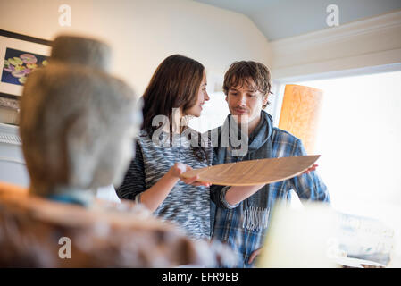 Lächelnde paar stehen in einem Wohnzimmer, Frau hält ein Holztablett. Stockfoto