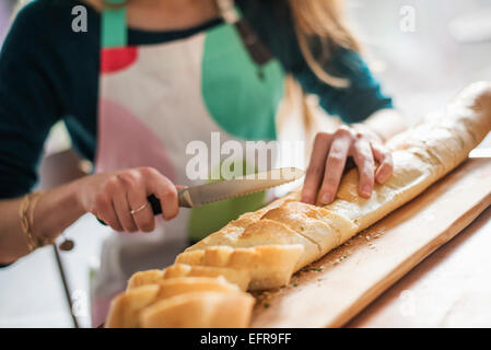 Nahaufnahme einer Frau trägt eine Schürze, sitzen an einem Tisch eine Baguette aufschneiden. Stockfoto