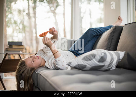 Mädchen auf einem Sofa auf dem Rücken liegend einen Papier Vogel hält. Stockfoto