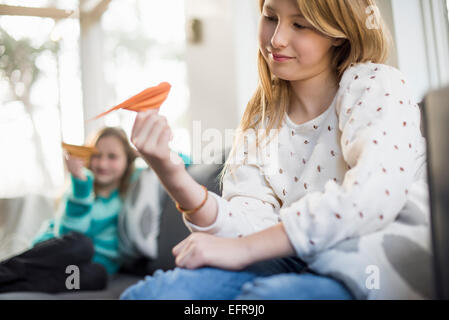 Zwei Mädchen sitzen auf einem Sofa, Papier Vögel halten. Stockfoto