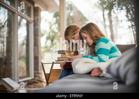 Zwei Mädchen sitzen auf einem Sofa, ein Buch zu lesen. Stockfoto