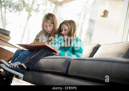 Zwei Mädchen sitzen auf einem Sofa, ein Buch zu lesen. Stockfoto