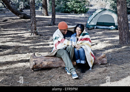 Camping Pärchen sitzt auf Log in Decke gehüllt Stockfoto