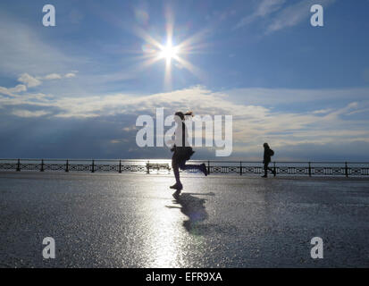 Ein weibliche Mädchen Jogger läuft Promenade Hove Rasen wirft ihre Schatten in der frühen Morgensonne am glitzernden Meer Stockfoto