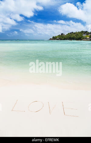 Das Wort Liebe in den Sand von einem sauberen weißen Strand mit türkisfarbenem Wasser geschrieben Stockfoto