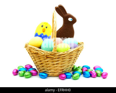 Osterkorb gefüllt mit bunten Eiern und Süßigkeiten über weiß Stockfoto