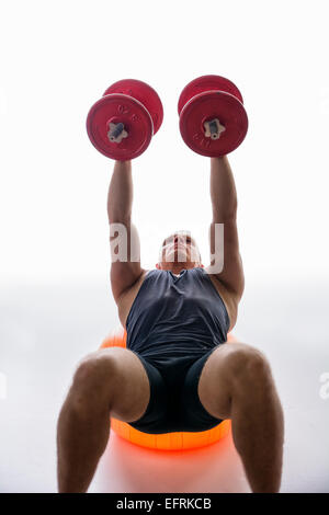 Sportlicher junger Mann Workout mit Hanteln auf Gymnastikball Stockfoto