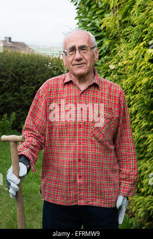 Älterer Mann stehend im Garten, tragen von Arbeitskleidung und Holding Spaten Stockfoto