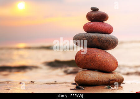 Steinen Pyramide auf Sand als Symbol für Zen, Harmonie und Balance. Meer bei Sonnenuntergang im Hintergrund Stockfoto