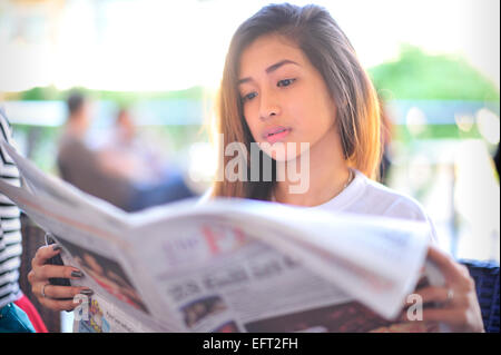 Filipina Schüler lesen Zeitung The Freeman in Bo es Coffee Shop auf den Terrassen im Ayala Center Cebu City Philippinen. Stockfoto