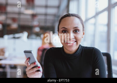Porträt der fröhliche junge Frau mit einem Mobiltelefon. Afrikanerin, Blick auf die Kamera zu Lächeln bei der Arbeit. Stockfoto